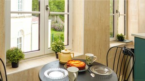 A small round table with a tea set, a plate, and a cup, positioned near a window with a view of a garden. - Cosy, bright 68m2 apartment in the center of town (Boulogne-sur-Mer)