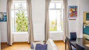A living room with a white sofa, a glass dining table, and two windows with curtains. - Cosy, bright 68m2 apartment in the center of town (Boulogne-sur-Mer)