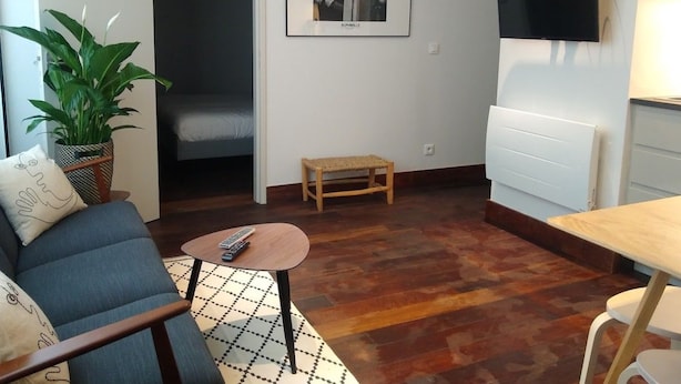 Una sala de estar con sofá, una mesita, una planta en maceta, un cuadro enmarcado y un televisor montado en la pared.