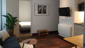 Un espacio habitable compacto con cama, una mesita, televisor y una planta en maceta.