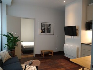 A compact living space with a bed, a small table, a television, and a potted plant. - Two Bedroom apartment in historical  center (Bordeaux)