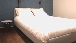 Una cama individual con ropa blanca en una habitación con paredes azules y una pequeña mesa redonda.