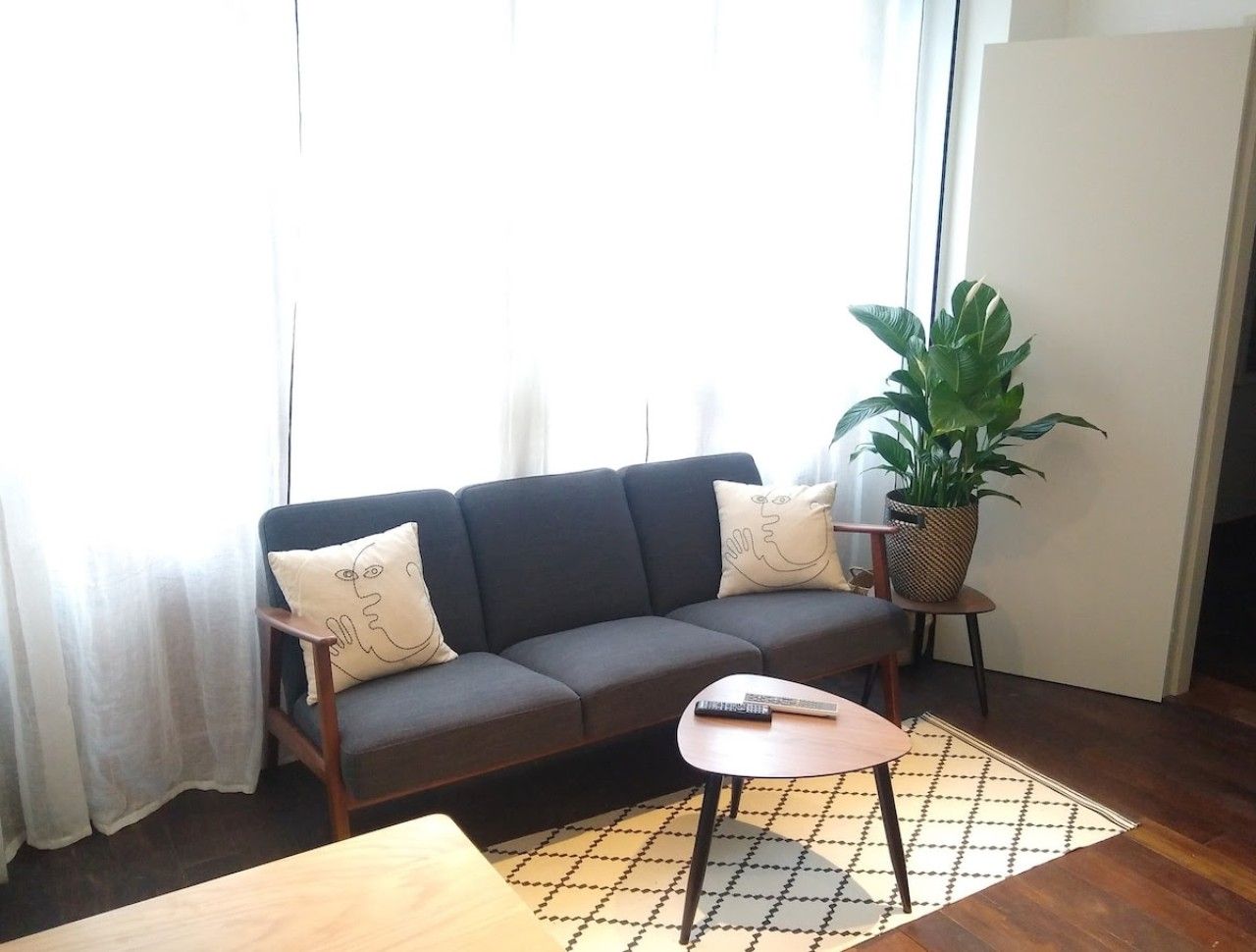 Una sala de estar con un sofá, una mesita, una planta en maceta y una ventana con cortinas.