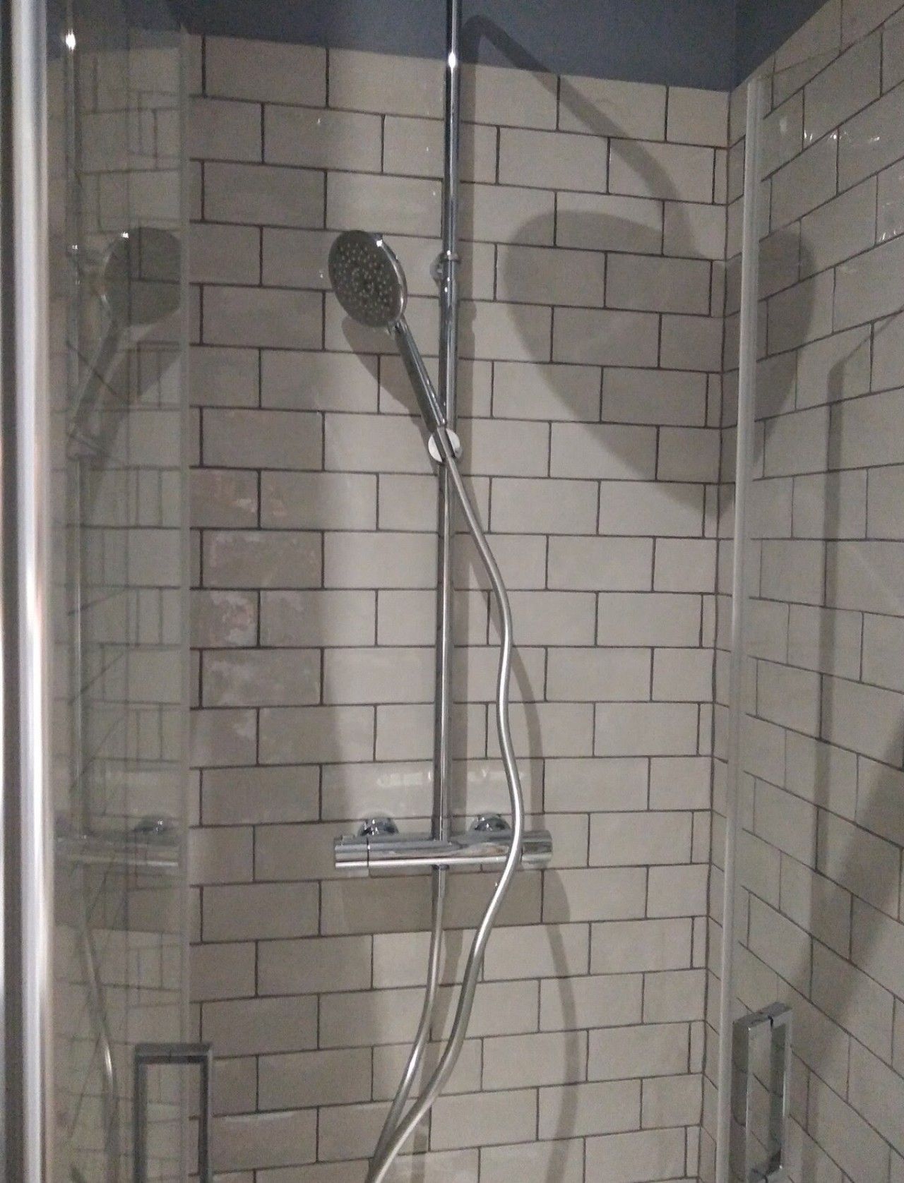 Une douche équipée d’un pommeau de douche à main et d’un robinet mural, le tout installé devant un mur carrelé.