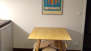 Una habitación pequeña con una mesa de madera y dos sillas, un refrigerador y un cartel colgado en la pared.