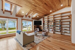 Een ruime woonkamer met een grote boekenkast, een open haard en uitzicht op zee.