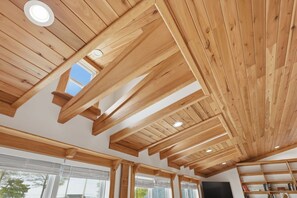 Een kamer met houten balken, grote ramen en een boekenplank.