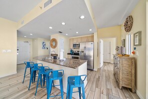 A spacious kitchen with a central island, blue bar stools, and a wooden cabinet. - Gulf Front/Chair Service/Heated Pool (Panama City Beach)