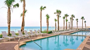 Un espace aménagé au bord de la piscine, avec des chaises longues et des palmiers, offrant une vue sur la mer.