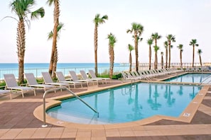 A pool area with lounge chairs and palm trees, overlooking the sea. - Gulf Front/Chair Service/Heated Pool (Panama City Beach)