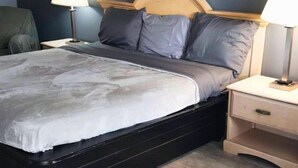 A bedroom with a bed, two bedside tables, a nightstand, and a chair. - 114 Gated King Bed Hotel Room (Jackson)