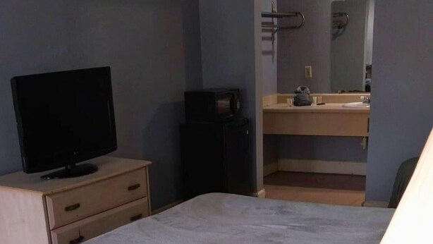 A bedroom with a bed, a TV on a bedside table, a dresser, and a bathroom with a mirror and sink. - 114 Gated King Bed Hotel Room (Jackson)