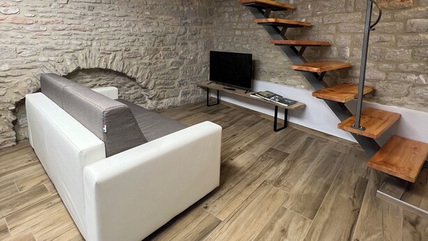 Ein modernes Wohnzimmer mit Steinwand, einem weißen Sofa, einem Flachbildfernseher und einer Holztreppe.