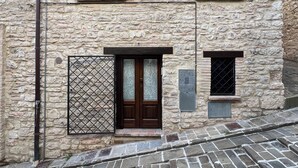 Ein Steinhaus mit einem zentralen Eingang, zwei Fenstern im oberen Stockwerk und einem kleinen Fenster auf der rechten Seite.