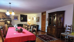 A dining area with a red tablecloth, wooden chairs, a chandelier, and a cabinet with glass doors. - Apartment in Villa Jolanda (Romano d'Ezzelino)