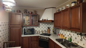 A kitchen with wooden cabinets, a microwave, a stove, and a sink. - Apartment in Villa Jolanda (Romano d'Ezzelino)