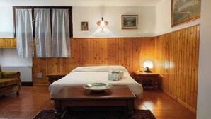 A room with a wooden paneled wall, a bed with a white mattress and pillows, a bedside table with a lamp, a small rug, and a framed picture on the wall. - Apartment in Villa Jolanda (Romano d'Ezzelino)
