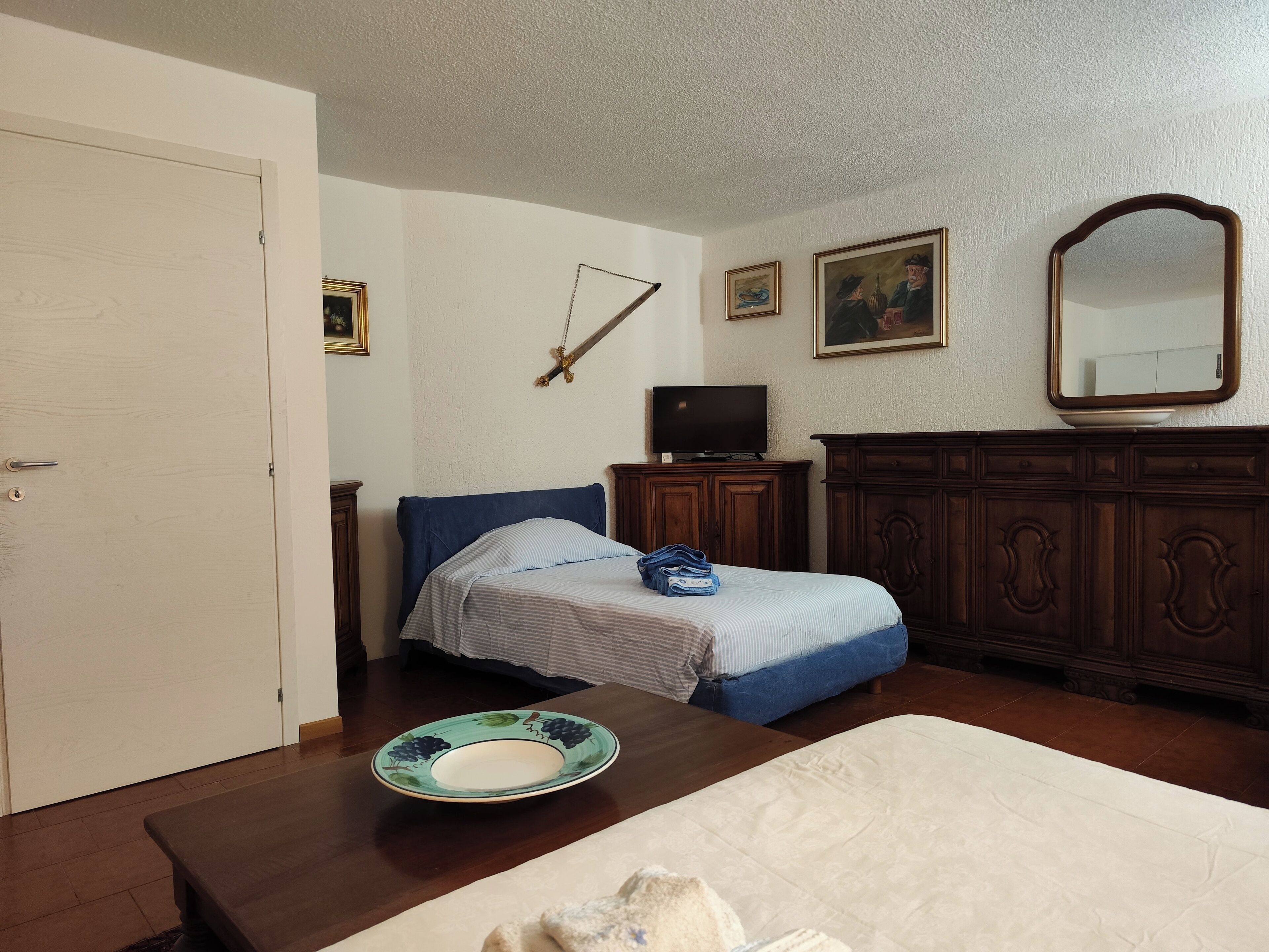 Um quarto com cama, cômoda, televisão e porta.