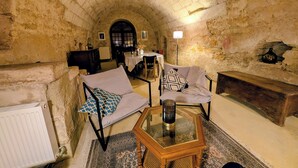 Una habitación con paredes de piedra y un techo alto en arco, una mesa de comedor con sillas, un sofá con cojines estampados, un banco de madera y una mesa con cubierta de vidrio y un jarrón decorativo.
