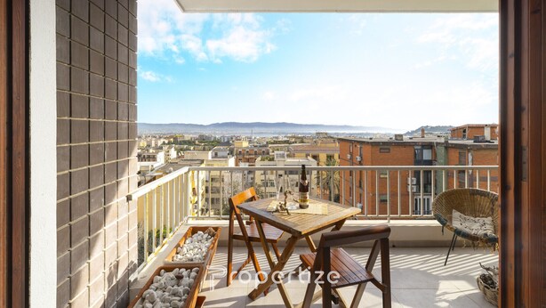 A balcony with a table and chairs, a wicker chair, and a view of the cityscape. - Cagliari panoramic view by Propertize (Cagliari)