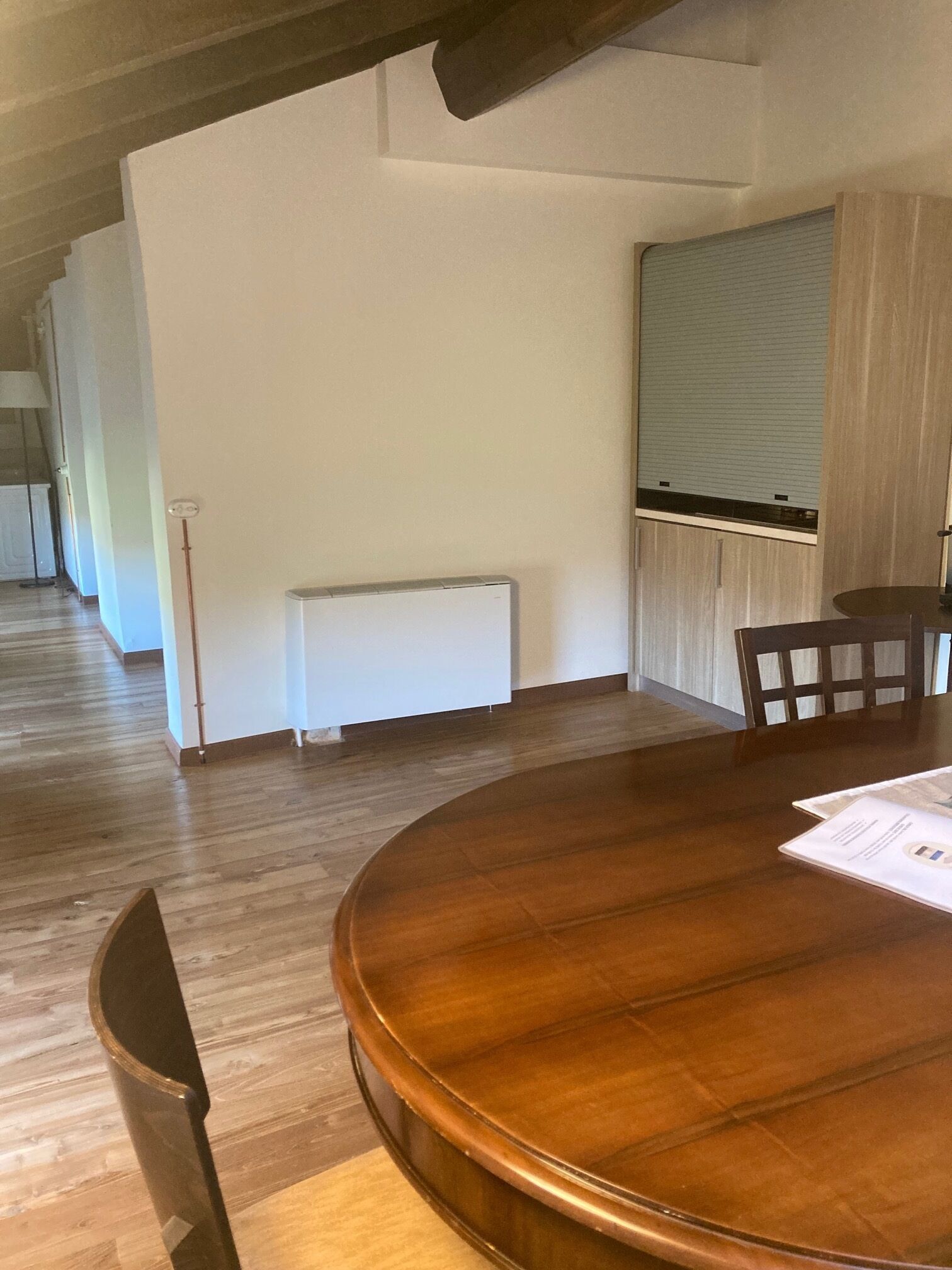 Un salón de conferencias con una mesa redonda de madera, paredes blancas y un radiador.
