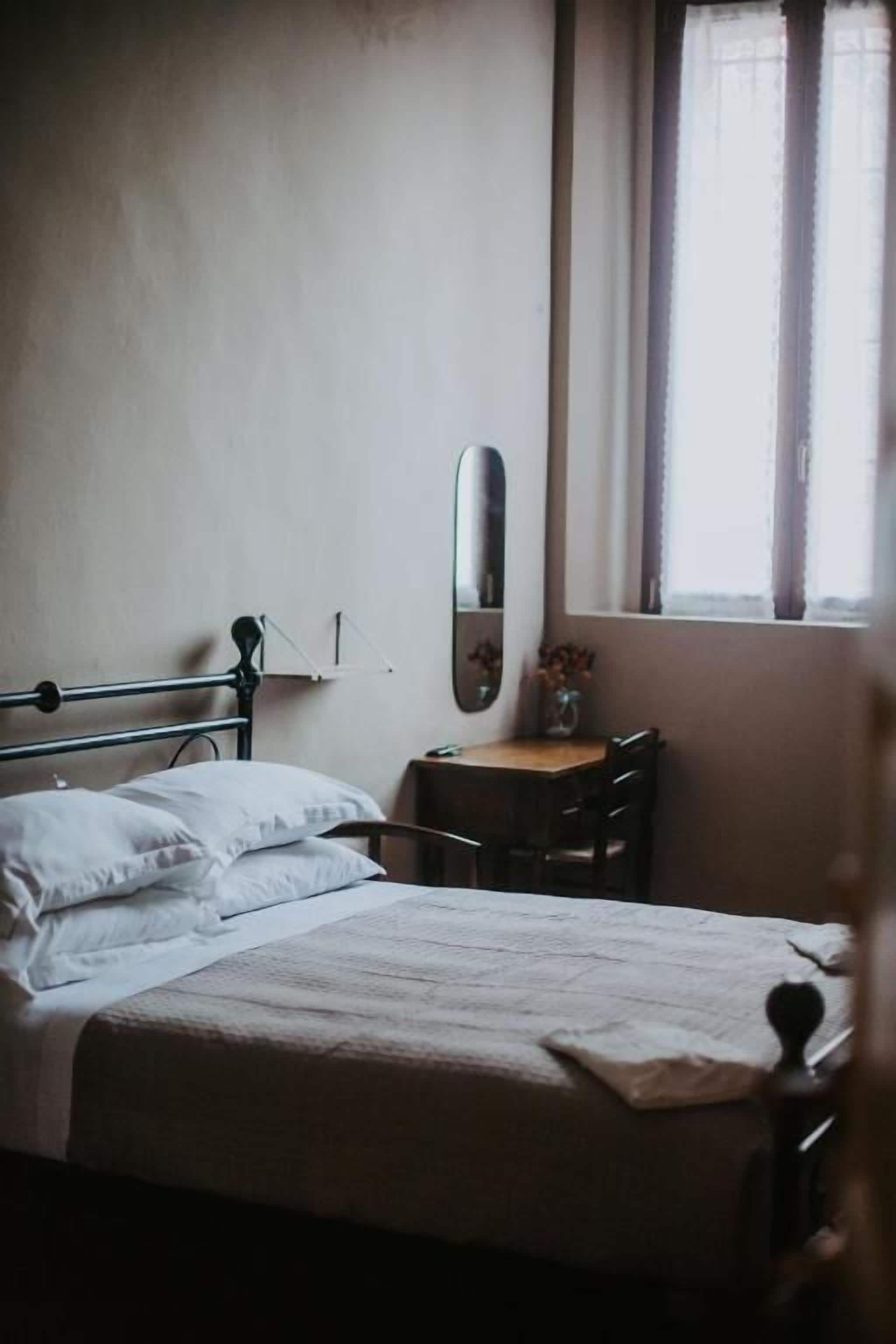 Ein Schlafzimmer mit Bett, Nachttisch, Spiegel und einem Fenster mit Vorhängen.
