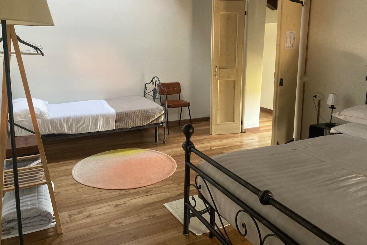 A room with two beds, a chair, a wooden floor, and a door leading to another room.
