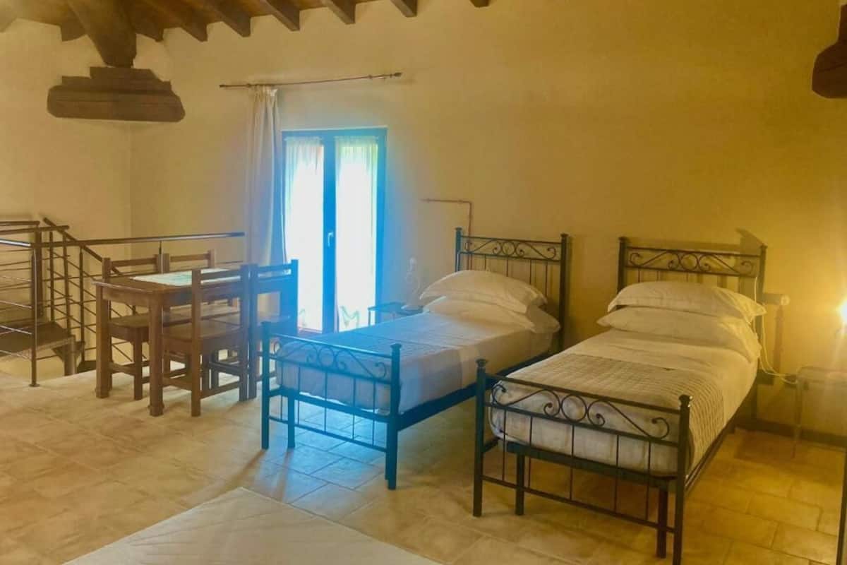 A bedroom with two beds, a wooden table, and a window with curtains.