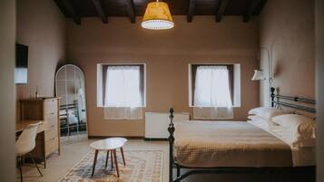 Un dormitorio con una cama, un escritorio, dos ventanas, un radiador y una lámpara colgante.