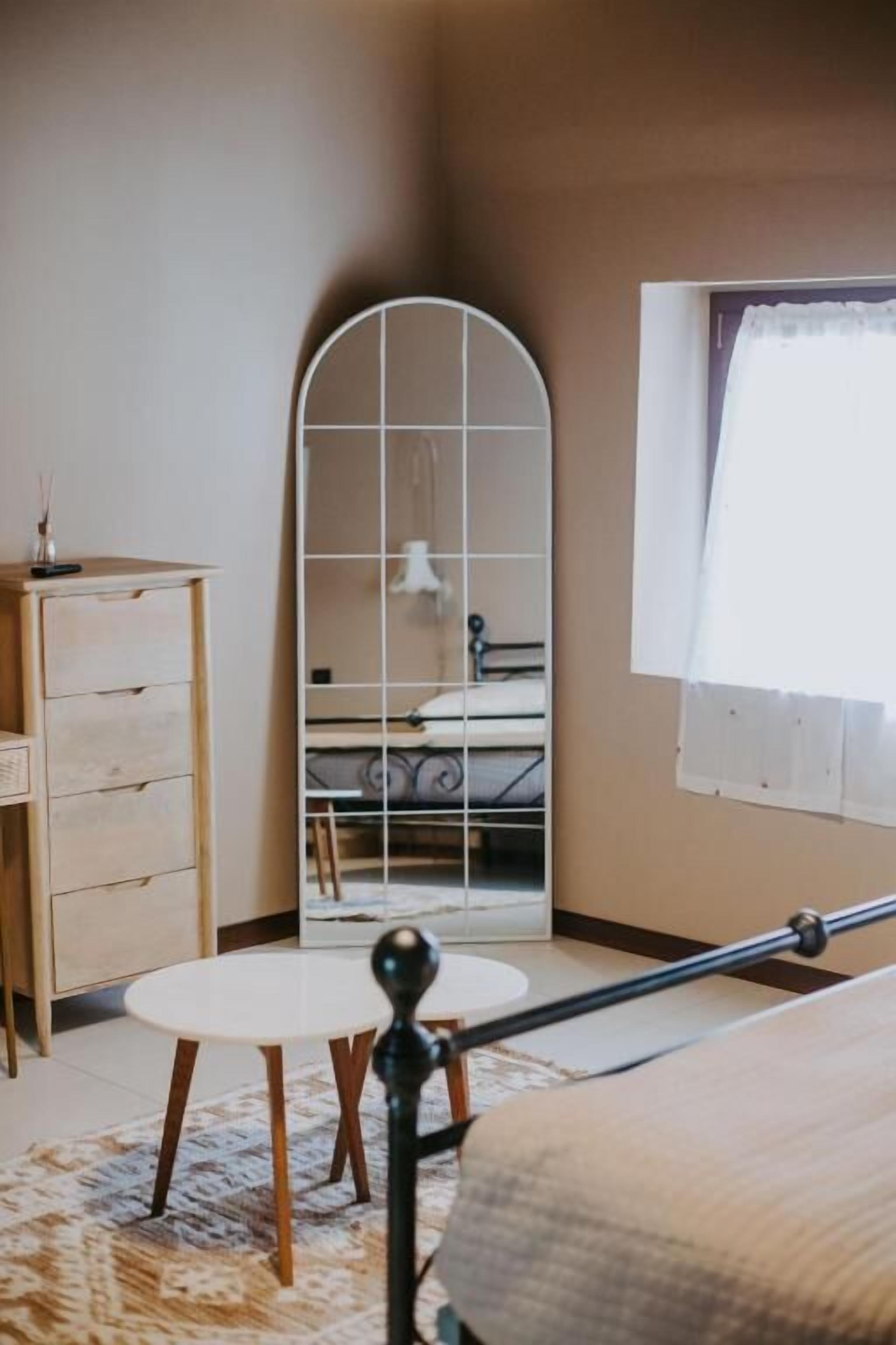 Un dormitorio con cama, cómoda, espejo y ventana con cortinas.