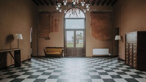 A room with a checkered floor, a sofa, a lamp, a cabinet with drawers, and a large window with a view. - Agriturismo Pizzavacca (Villanova sull'Arda)