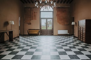Una habitación con piso a cuadros, un sofá, una lámpara, un mueble con cajones y un ventanal con vistas.