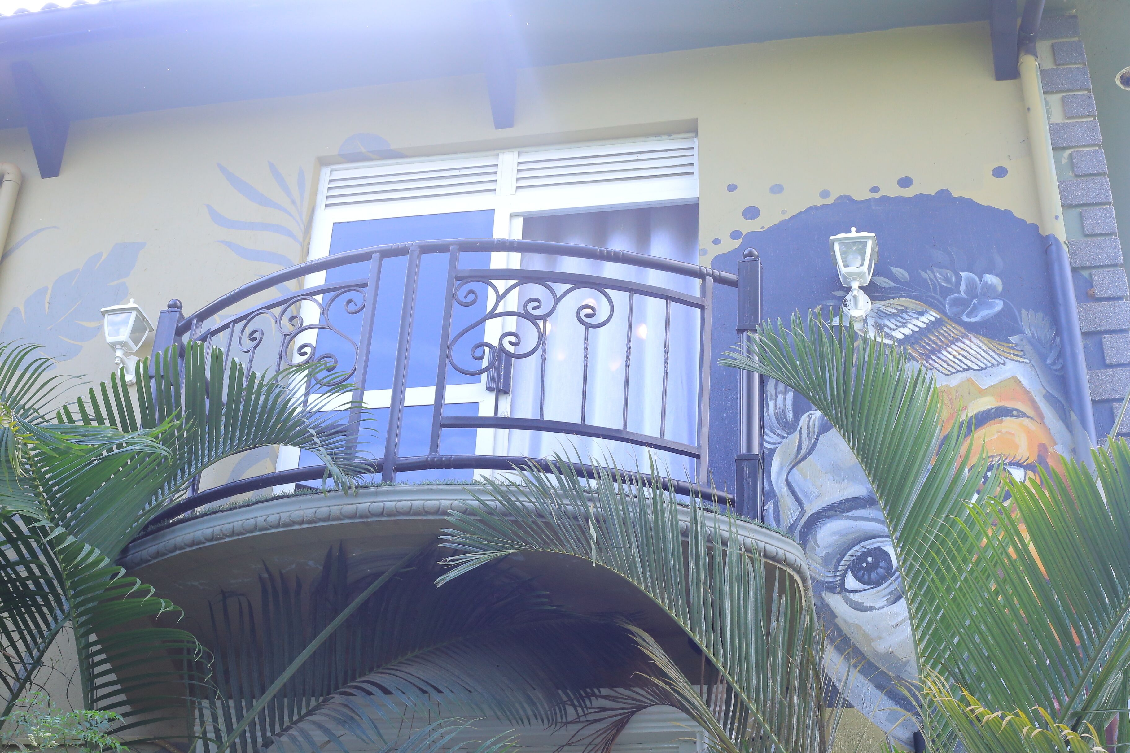 A balcony with a wrought iron railing, a small circular table, and a mural on the wall.