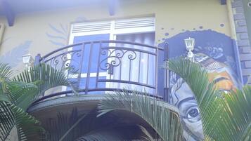 A balcony with a wrought iron railing, a small circular table, and a mural on the wall.