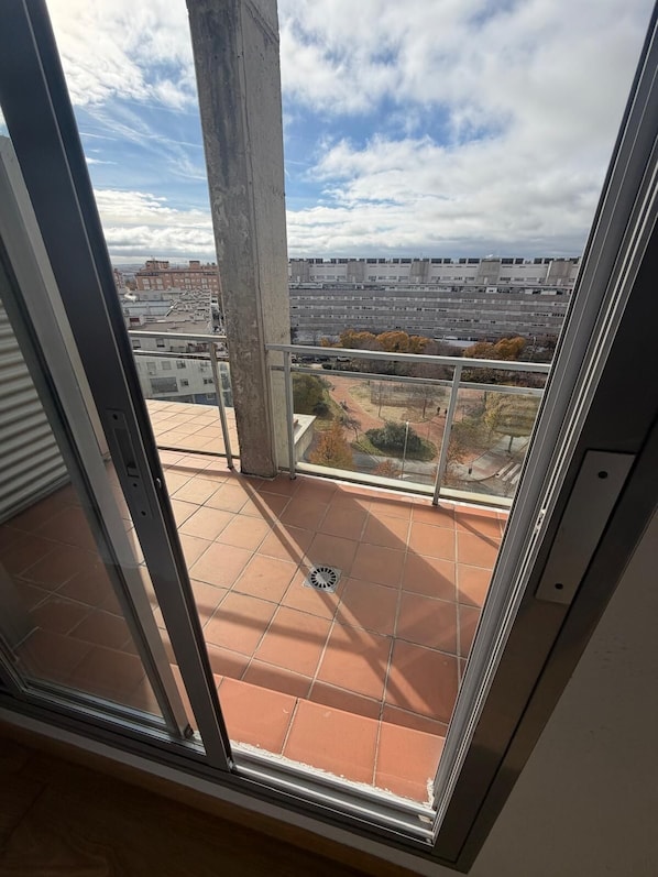 A balcony with a view of a cityscape, a concrete pillar, and a tiled floor. - Apartament H&C (Madrid)