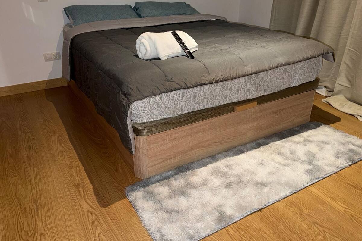 A bedroom with a bed, a wooden floor, a grey rug, and a grey headboard.