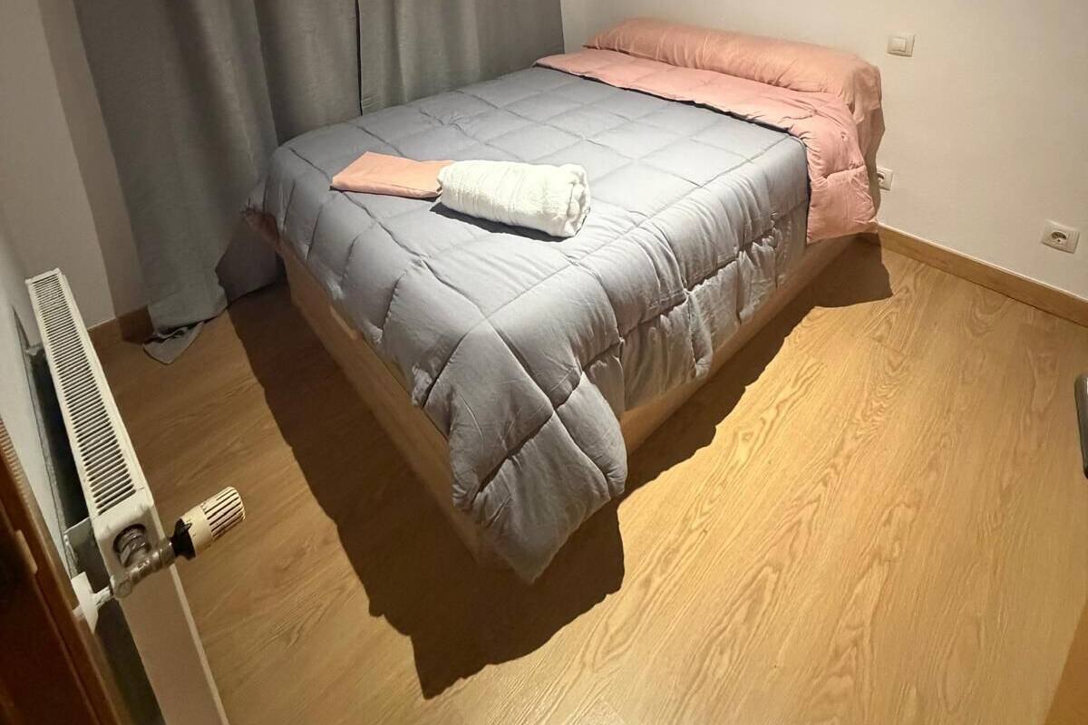A small, neatly arranged bedroom with a bed, a radiator, and a window with curtains.