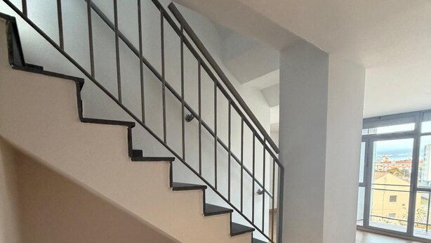 A staircase with a metal railing leading to a landing. The landing area has a wooden floor and a large window offering a view of buildings outside. - Apartament H&C (Madrid)