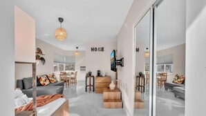 Un saló modern amb un sofà, una taula de centre i un televisor fixat a la paret. Hi ha una escala que condueix a un altre pis, i una zona de dinar amb cadires i taula.