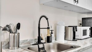 Una cucina moderna con lavello in acciaio inossidabile, rubinetto nero, macchina del caffè e forno a microonde.