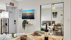 Un soggiorno moderno con zona pranzo, TV a parete e vista sulla camera da letto tramite una porta scorrevole.