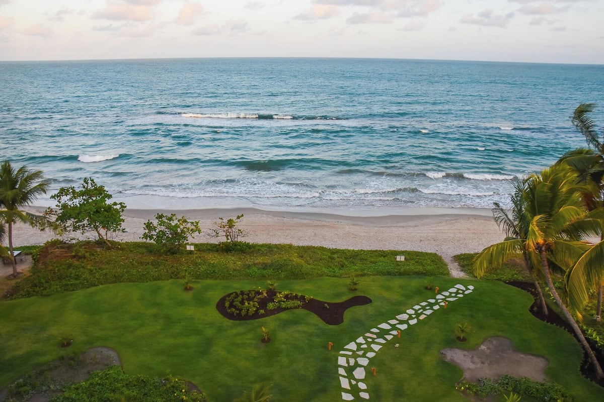 A coastal landscape with a beach, ocean, and a well-maintained garden with a stone pathway.