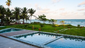 Zona de piscina con vistas al océano, rodeada de palmeras y un césped cuidado.