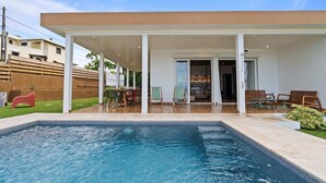 Een modern huis met een zwembad, overdekt terras en uitzicht op de achtertuin.