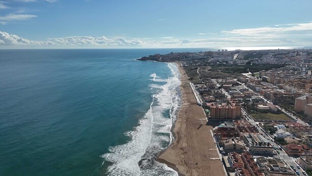Vista aérea de una ciudad costera con playa, edificios y cielo despejado.