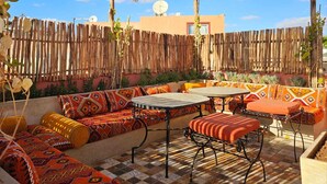 An outdoor patio with a thatched roof, wicker hanging lamps, and a variety of colorful cushions and rugs. - 3-bedroom Riad in enchanting Marrakech, Wifi and Pool (Marrakech)