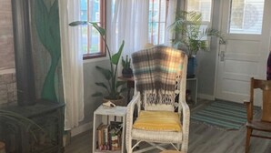 A cozy living room with a wicker chair, a small side table with books, a potted plant, and a woven rug. - Lake Life for Two -Walk to Marina + Close to Beach (Lakeview)