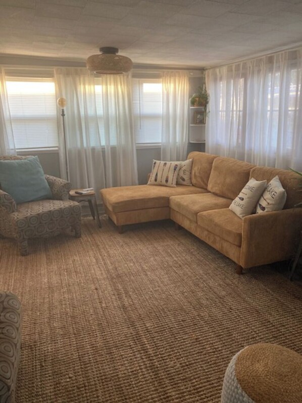 Un salon avec un canapé d’angle beige, un fauteuil à motifs et une petite table d’appoint.