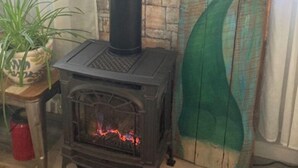 A wood-burning stove with a chimney, a hanging plant, and a wooden wall with a green mermaid tail mural. - Lake Life for Two -Walk to Marina + Close to Beach (Lakeview)