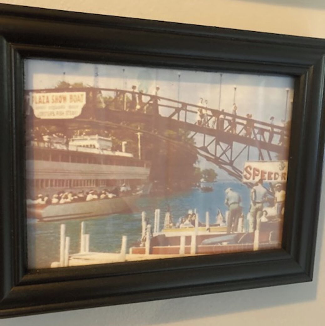 A framed picture of a historic bridge with a boat and people.